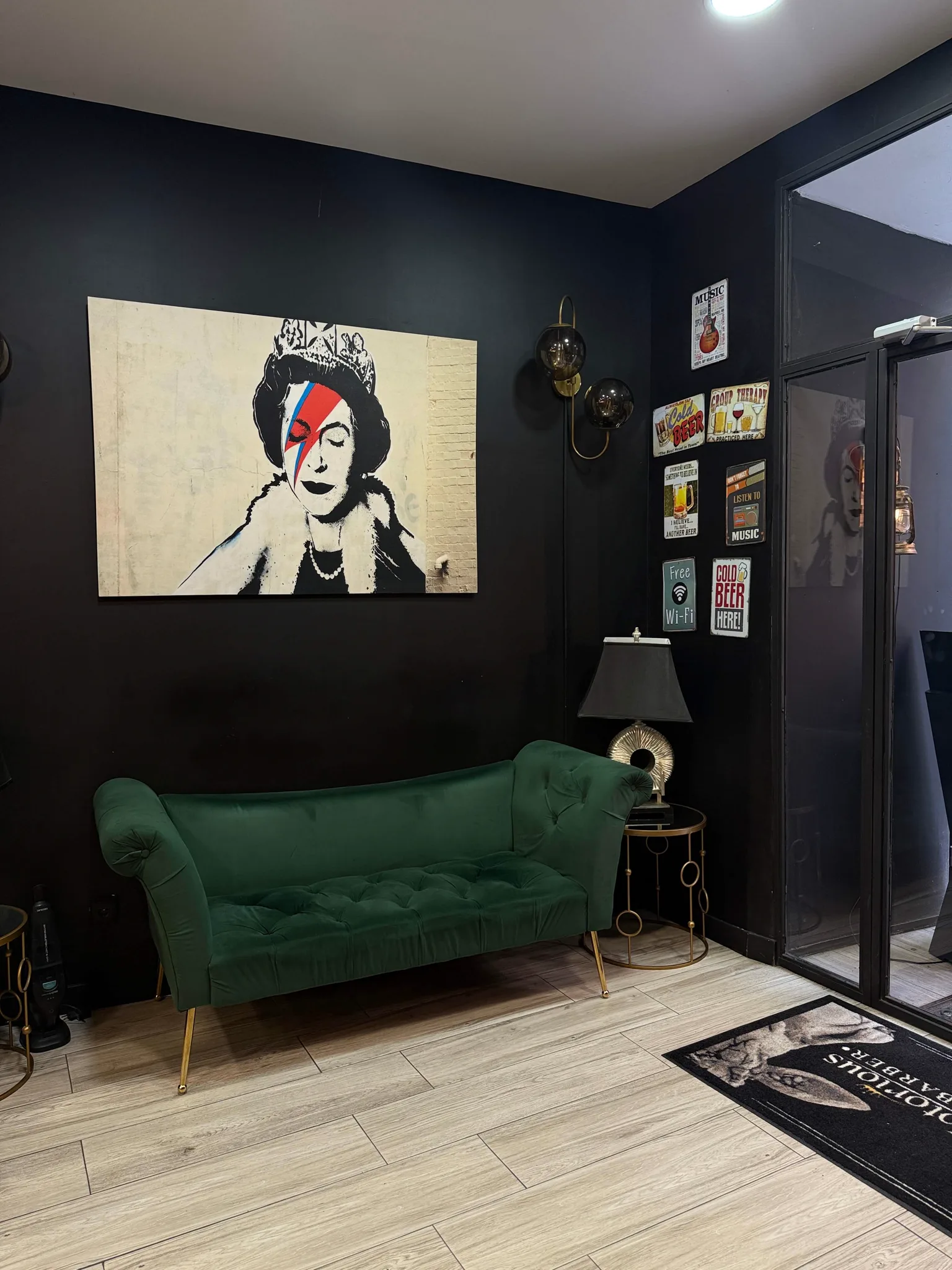 Sala de espera: sofá verde, cuadro de la reina y rótulo de la barbería